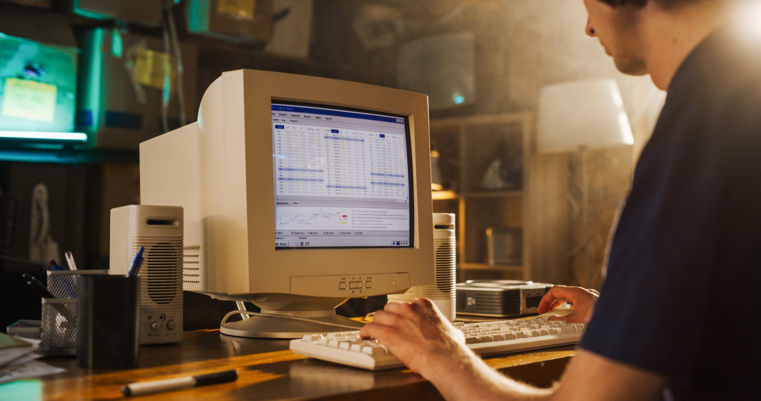 Male Stock Trader Using Old Desktop Computer With Financial Candlestick Chart In Retro Garage. Man Analyzing Market Orders Before Entering Trade, Starting Investment Fund In Nineties